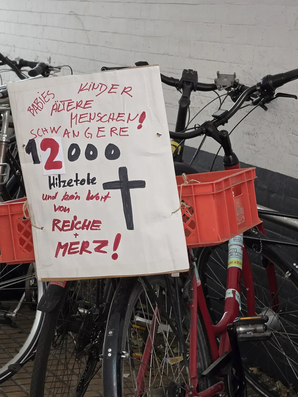 Pancarta con el texto «Babies, Kinder, ältere Menschen, Schwangere! 12000 Hitzetote und kein Wort von Reiche + Merz!», fotografiada en Hamburg, Alemania.
