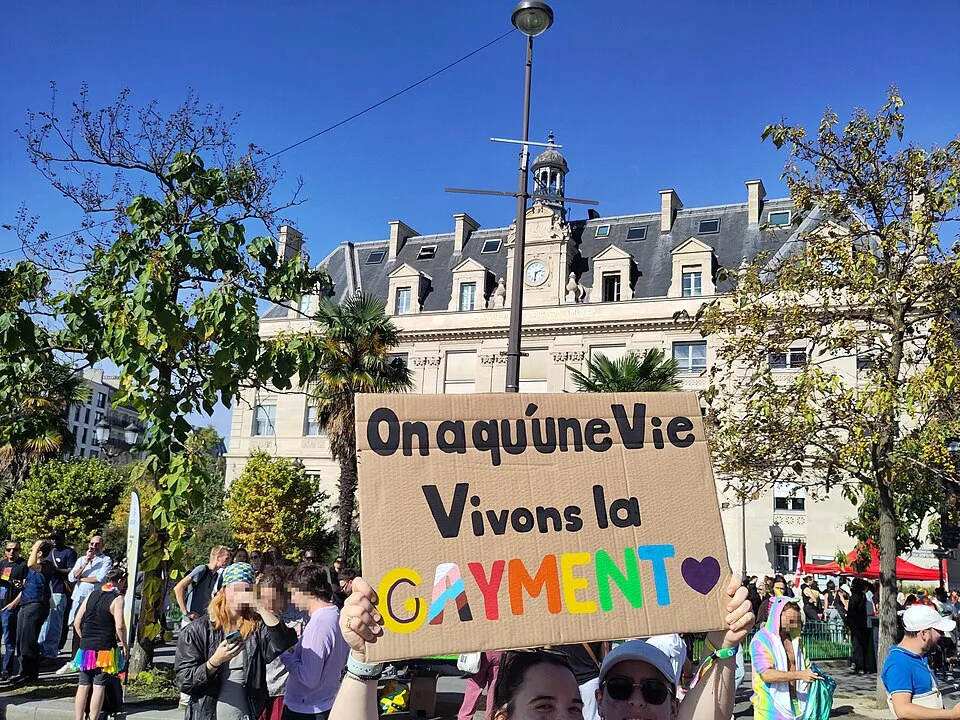 Protest sign reading “On a qu’une vie, vivons-la gayment” at “Paris Pride — 3 October 2026” in Paris, France.