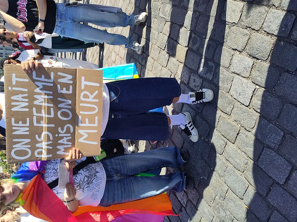 Protest sign reading “On ne naît pas femme mais on en meurt” at “Paris Pride — 3 October 2026” in Paris, France.