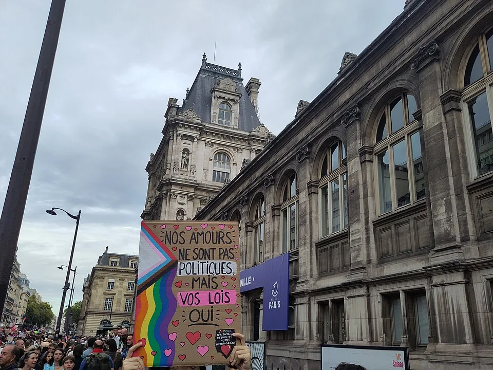 Protest sign reading “Nos amours ne sont pas politiques, mais vos lois, oui” at “Paris Pride — 3 October 2026” in Paris, France.