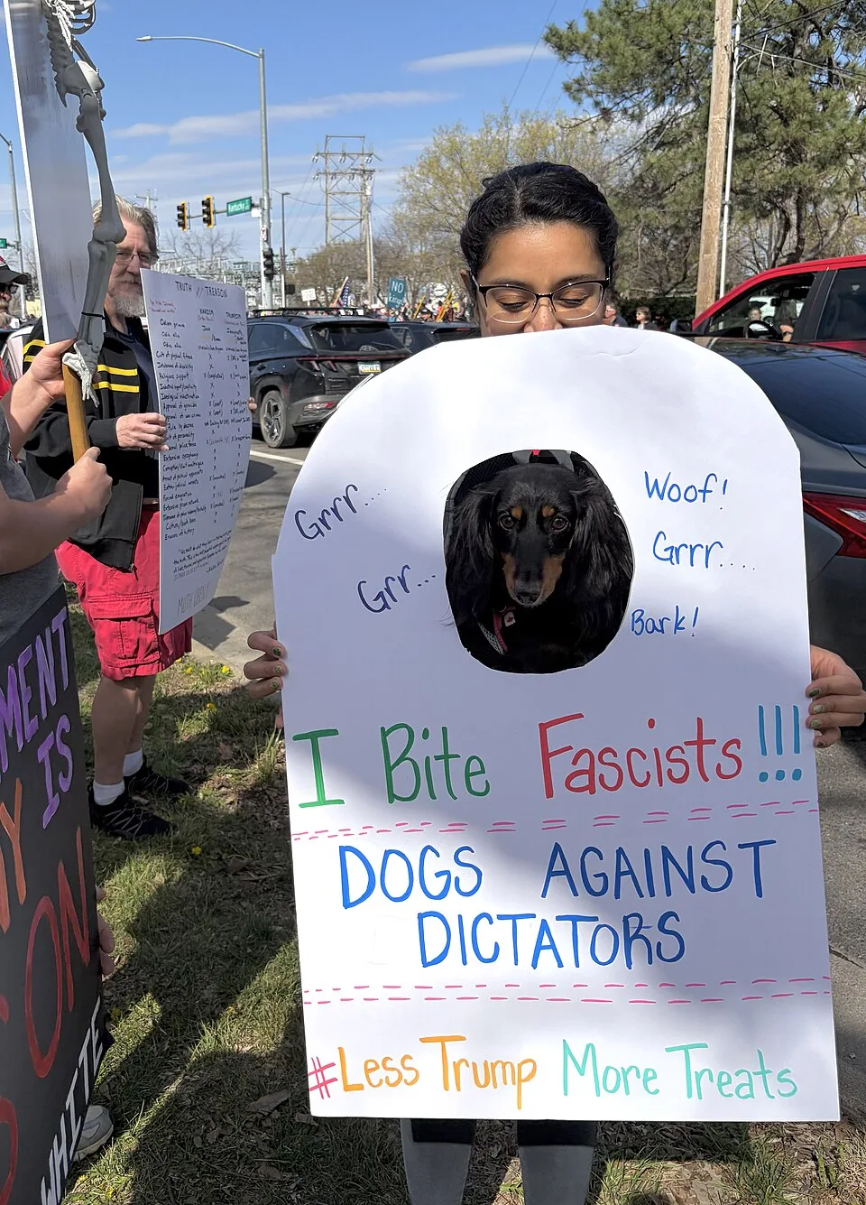 Protest sign reading “I bite fascists!!! Dogs against dictators. Less Trump, more treats” at “No Kings in Lawrence — 28 March 2026” in Lawrence, United States.