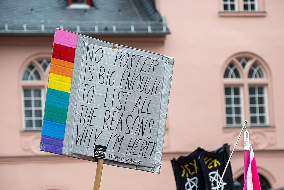 Pancarta con el texto «No poster is big enough to list all the reasons why I'm here!», fotografiada en Wiesbaden, Alemania.