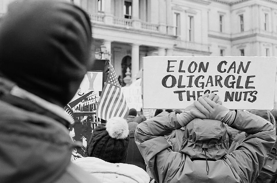 Protest sign reading “Elon can oligargle these nuts”