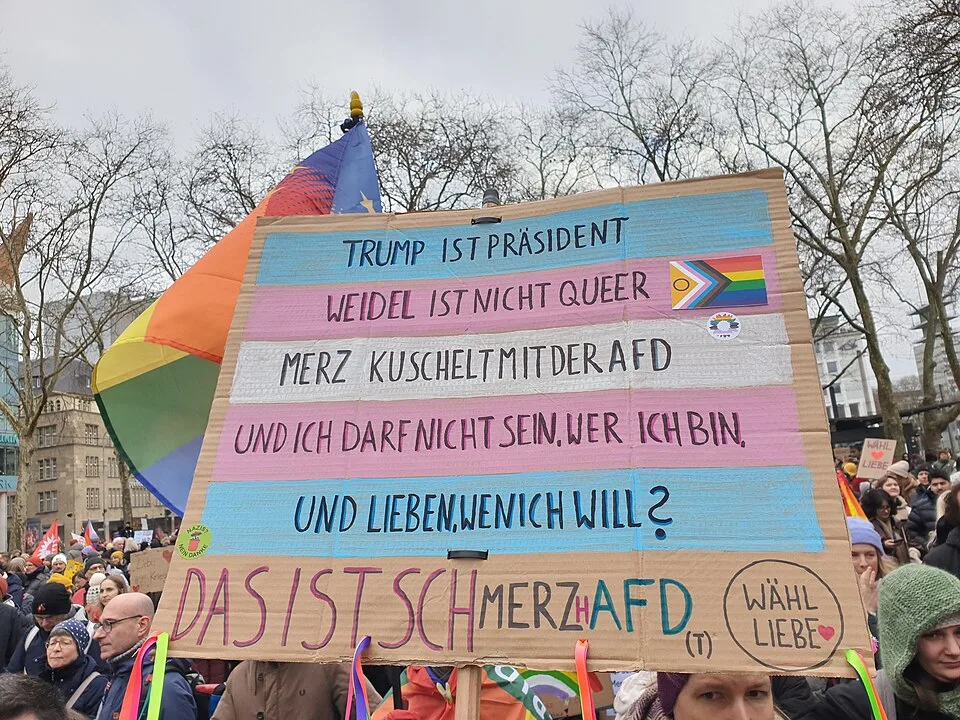 Pancarta con el texto «Trump ist Präsident, Weidel ist nicht queer, Merz kuschelt mit der AfD, und ich darf nicht sein, wer ich bin, und lieben, wen ich will? Das ist schMERZhAfD», fotografiada en Köln, Alemania.