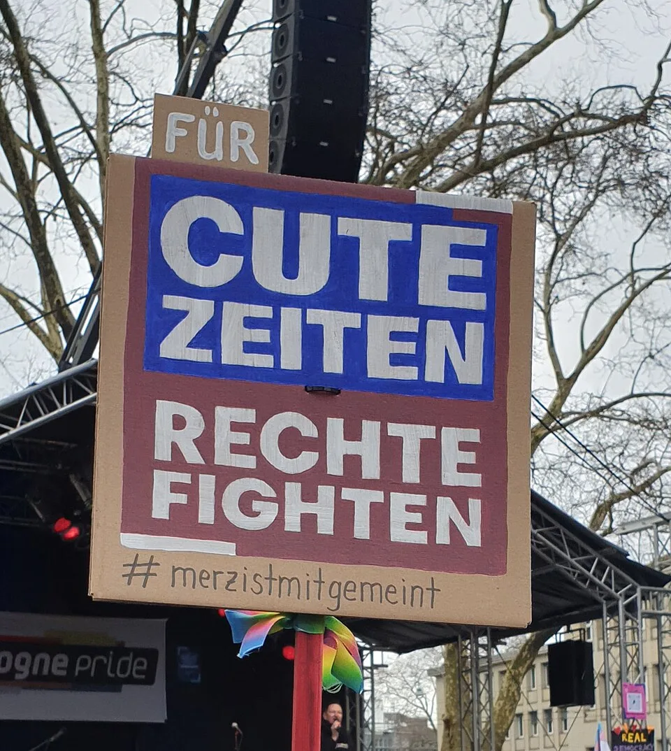 Pancarta con el texto «Für Cute Zeiten Rechte Fighten. #merzistmitgemeint», fotografiada en Köln, Alemania.