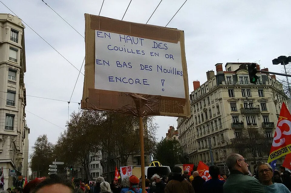 لافتة مظاهرة كُتب عليها «En haut des couilles en or, en bas des nouilles encore !»، صُوّرت في Lyon, فرنسا.