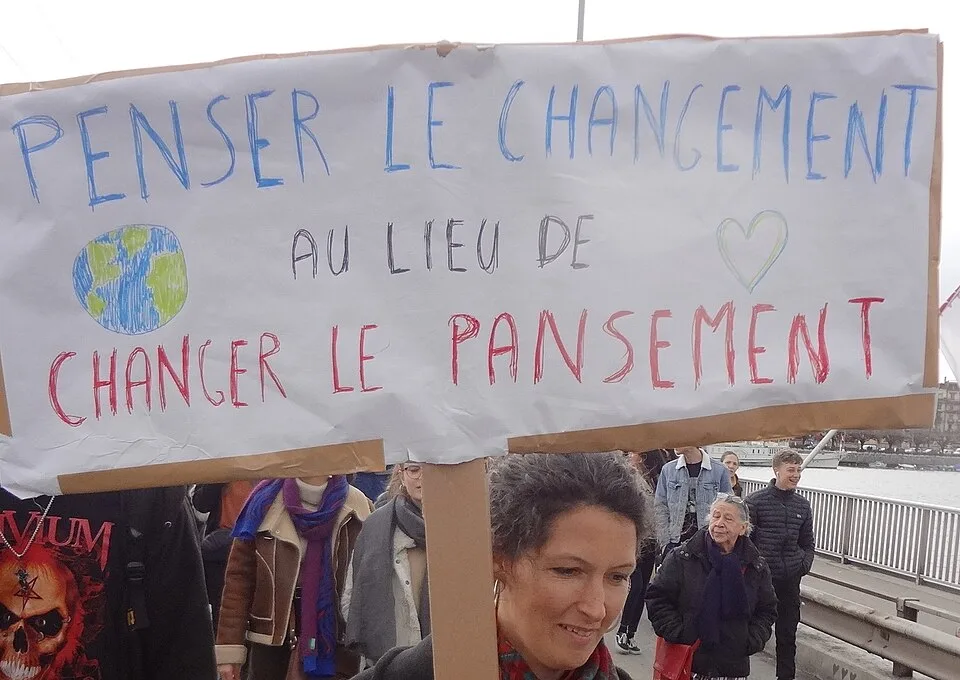 لافتة مظاهرة كُتب عليها «Penser le changement au lieu de changer le pansement»، صُوّرت في Genève, سويسرا.