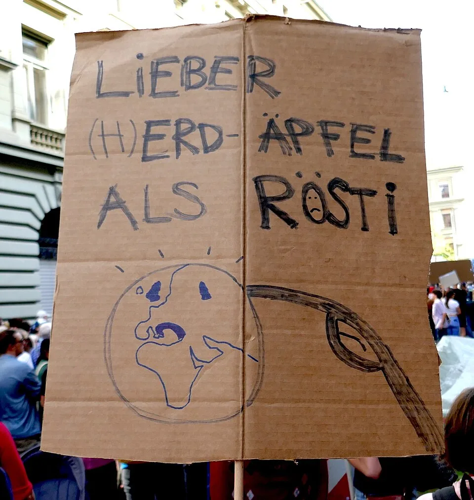لافتة مظاهرة كُتب عليها «Lieber (H)erd-Apfel als Rösti»، صُوّرت في Bern, سويسرا.
