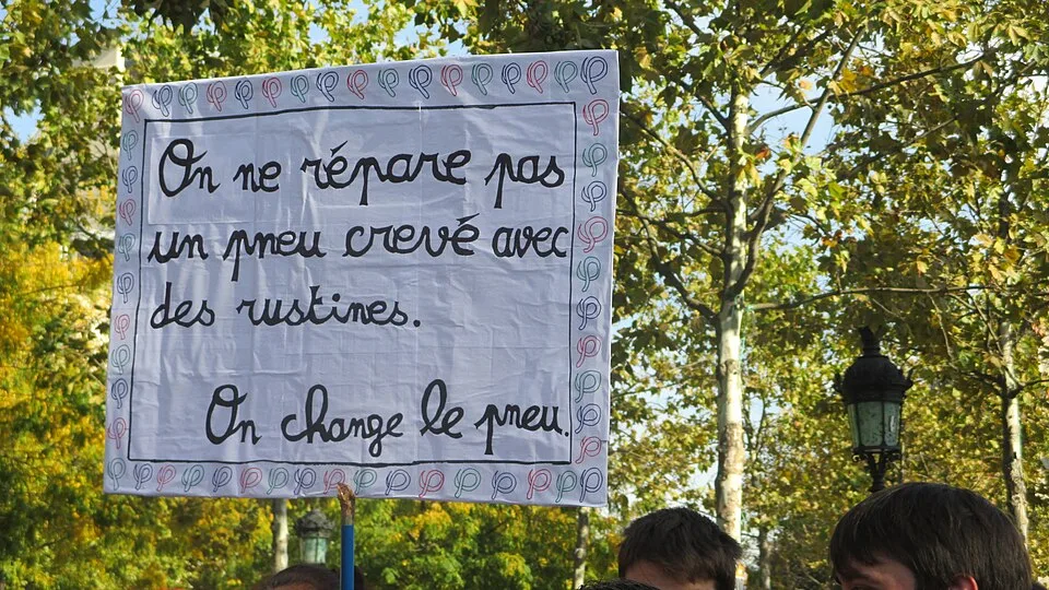 Pancarta de protesta que dice «On ne répare pas un pneu crevé avec des rustines. On change le pneu.»