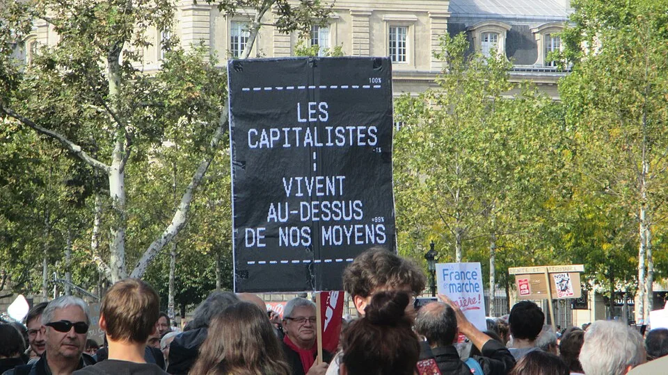 Protestbord met de tekst “Les capitalistes vivent au-dessus de nos moyens”