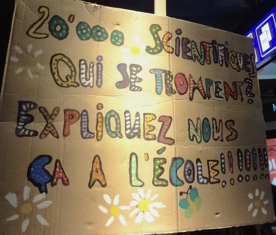 Pancarta con el texto «20 000 scientifiques qui se trompent ? Expliquez-nous ça à l'école !», fotografiada en Bern, Suiza.