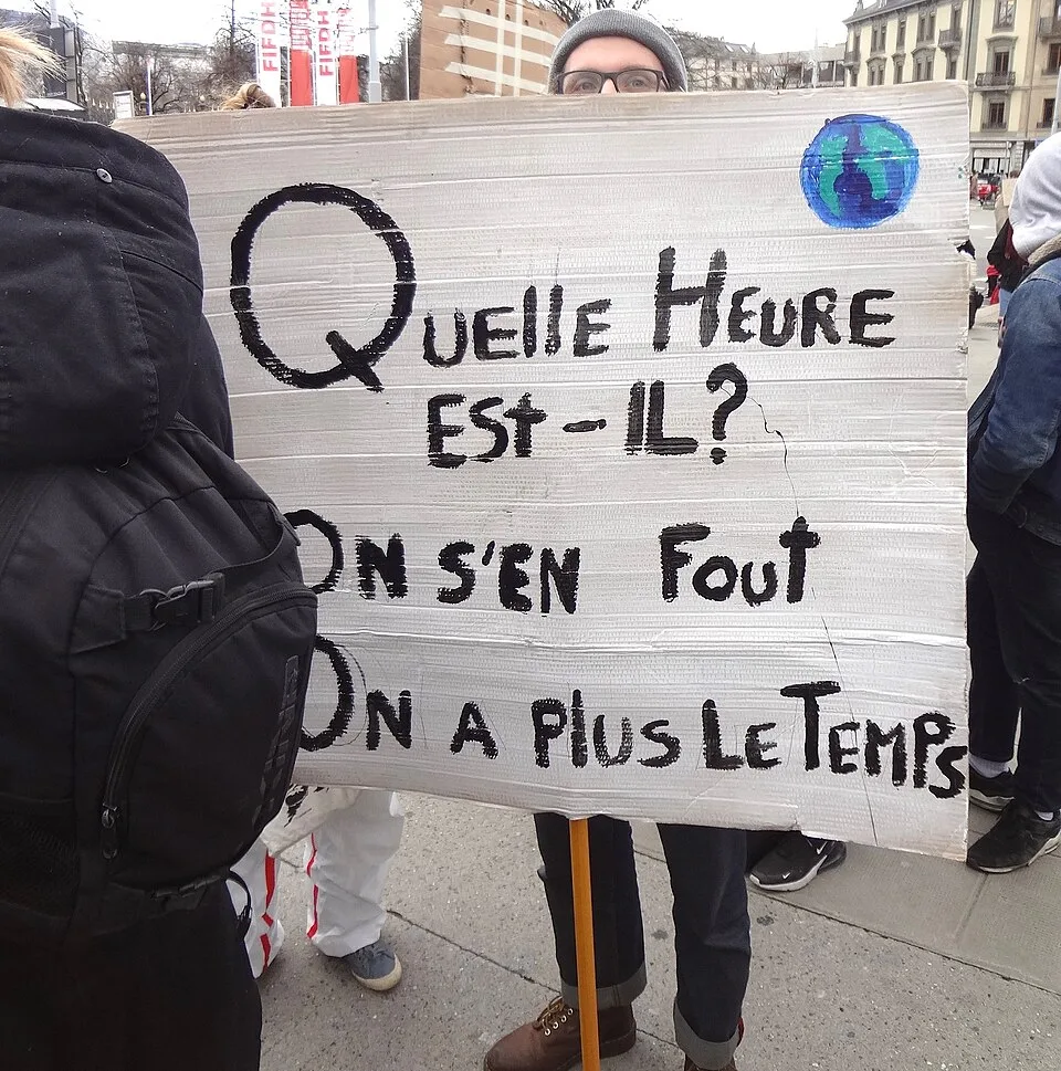 Pancarta con el texto «Quelle heure est-il ? On s'en fout, on n'a plus le temps», fotografiada en Genève, Suiza.