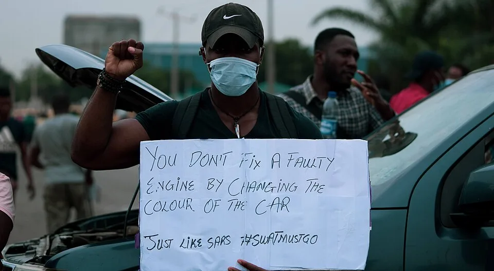 لافتة احتجاج مكتوب عليها «You don't fix a faulty engine by changing the colour of the car. Just like SARS. #SWATMUSTGO»