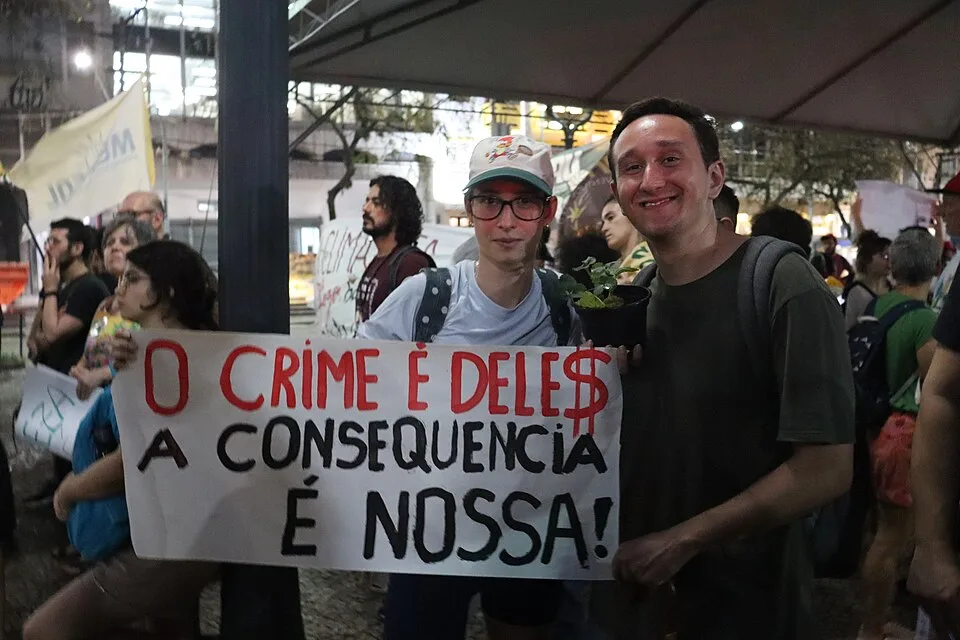 Pancarta de protesta que dice «O crime é dele$. A consequência é nossa!»