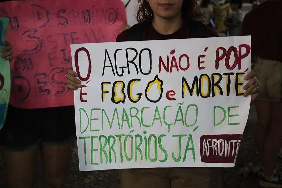 Pancarta de protesta que dice «O agro não é pop, é fogo e morte. Demarcação de territórios já»