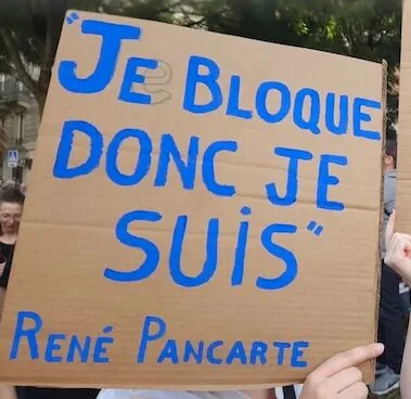 Protest sign reading “JE BLOQUE, DONC JE SUIS.”, photographed in France.