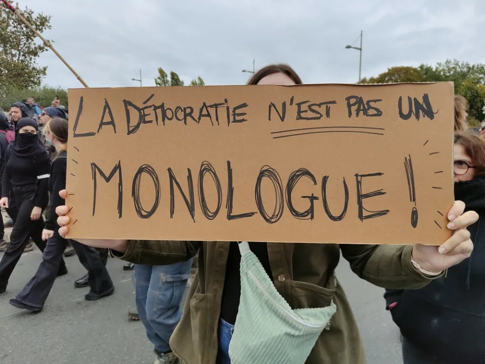 لافتة كُتب عليها «La démocratie n’est pas un monologue !» خلال «Manifestation du 24 octobre 2026 en France» في Poitiers, فرنسا.