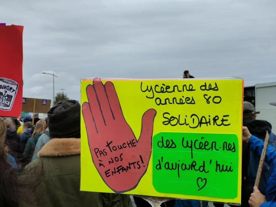 لافتة كُتب عليها «Lycéenne des années 80 solidaire des lycéen.nes d’aujourd’hui. Pas touche à nos enfants !» خلال «Manifestation du 24 octobre 2026 en France» في Poitiers, فرنسا.